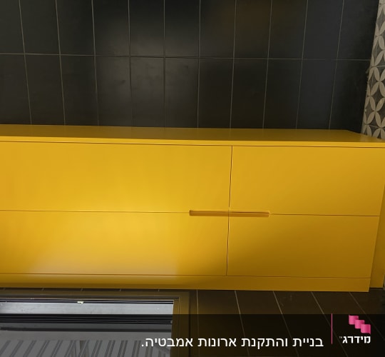 ארון צהוב עם ידית עץ על קיר שחור